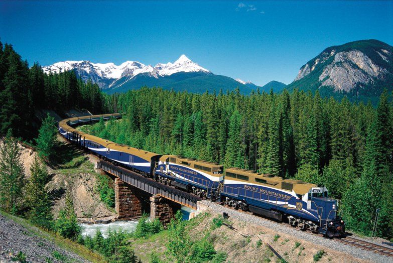 A train is going over a bridge with mountains in the background.