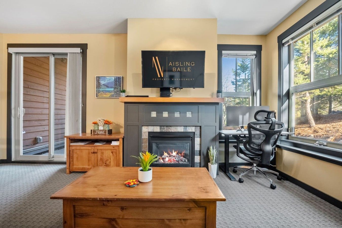 Bright living room with fireplace, wooden coffee table, large windows, and black office chair by the desk