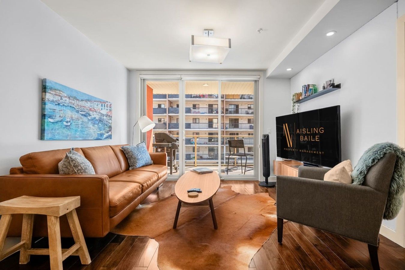 Bright living room with tan sofa, armchair, coffee table, floor lamp, TV, and large sliding doors.