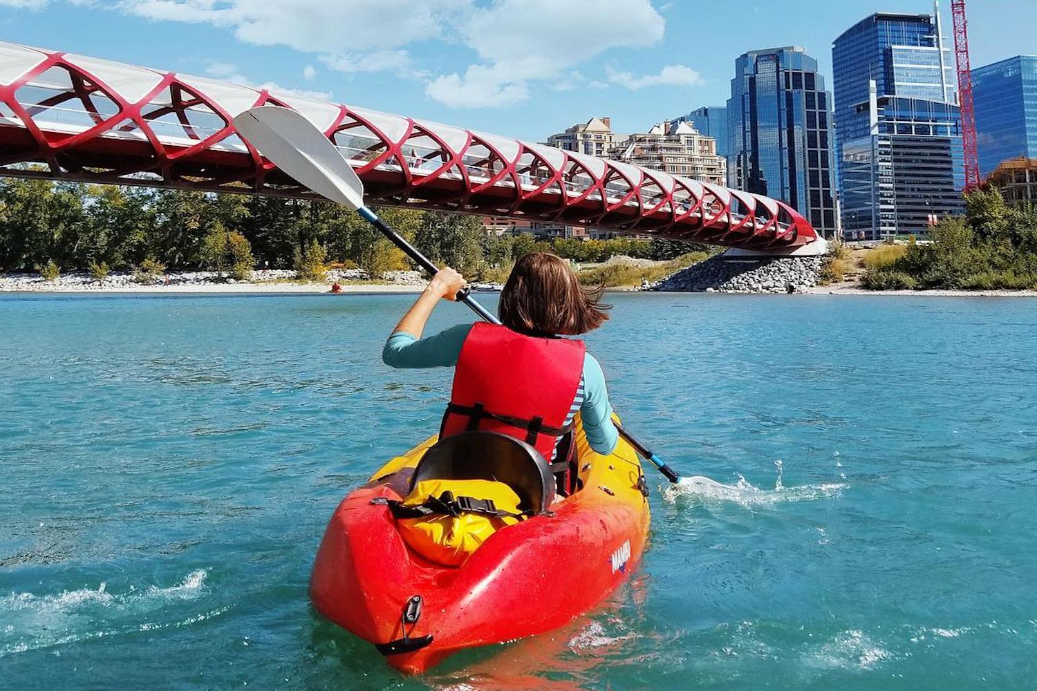 A woman is paddling a red kayak on a river.