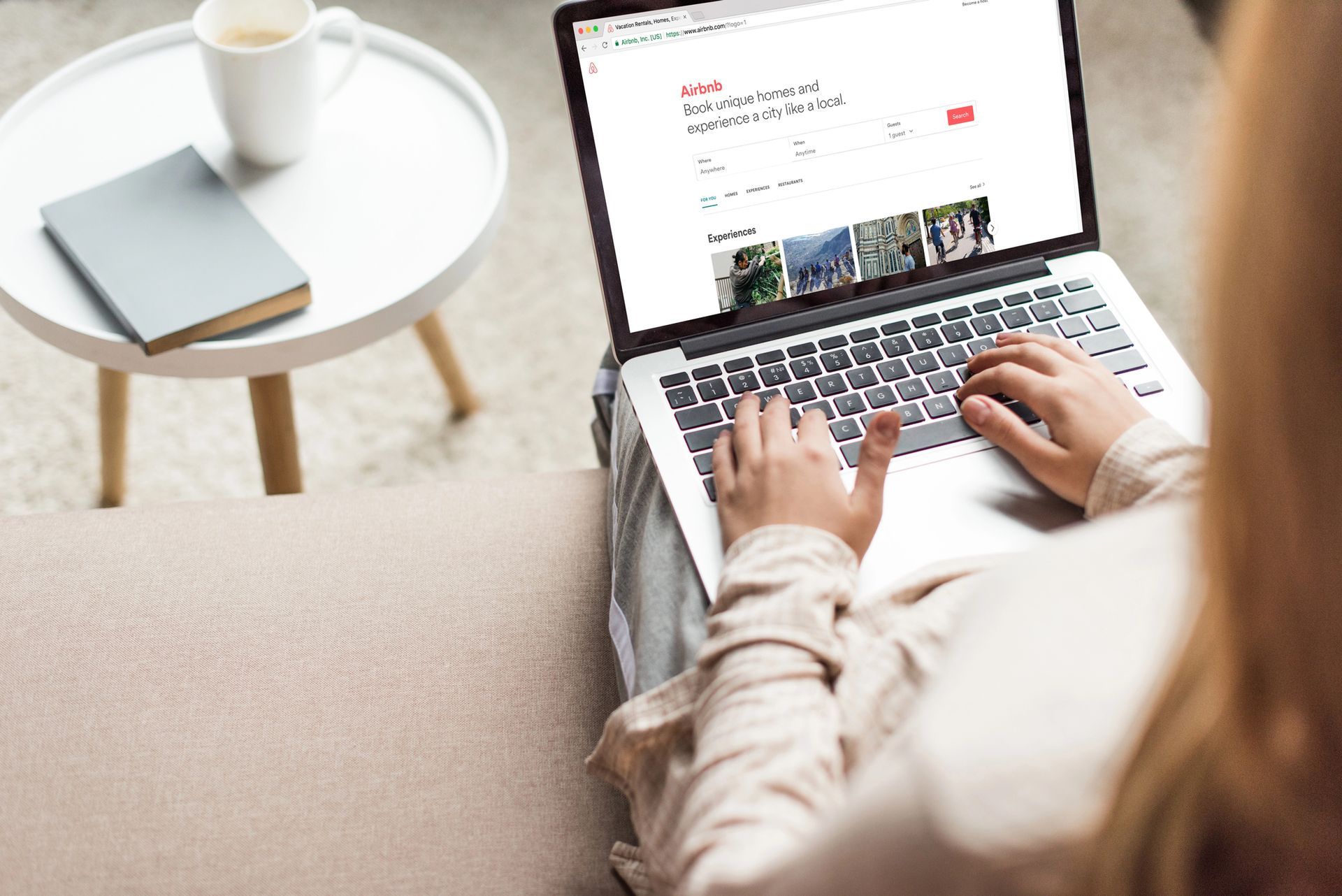 Person using a laptop on a couch beside a small table with a mug and notebook