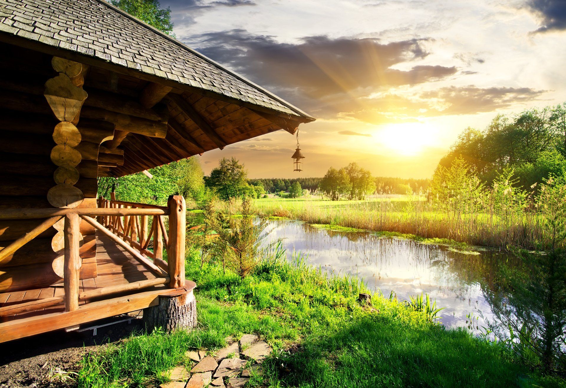 A log cabin is sitting next to a river at sunset.