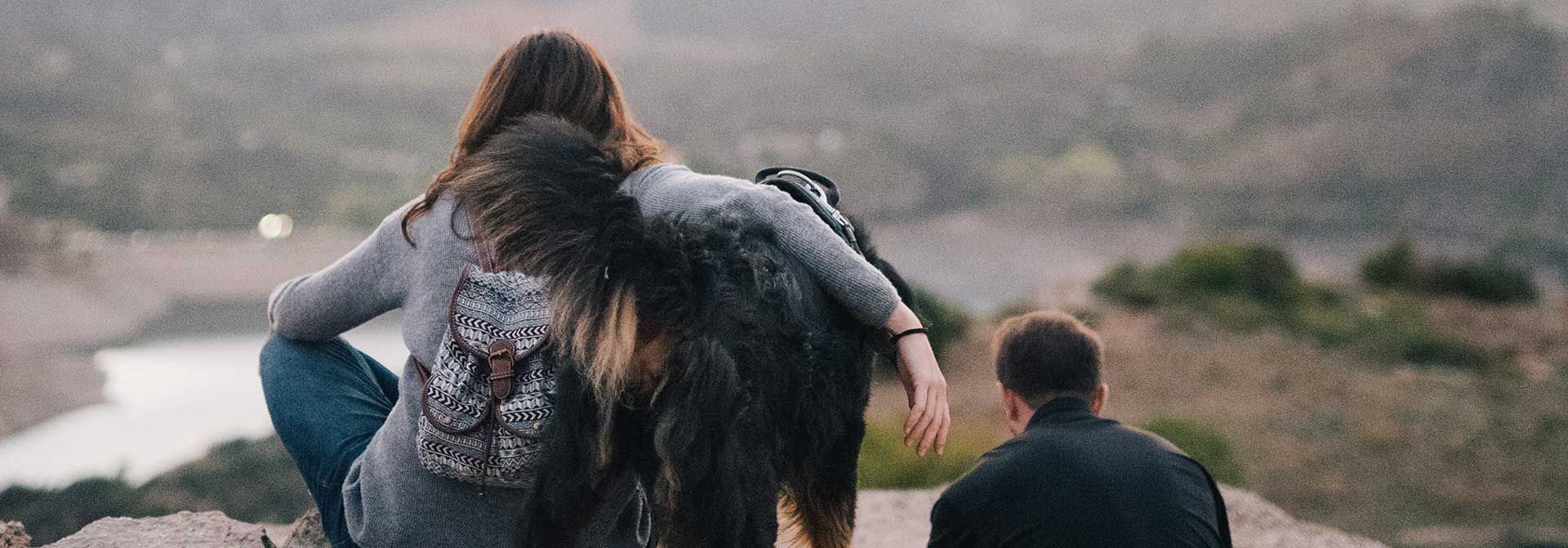 A group of people are sitting on top of a hill with a dog.