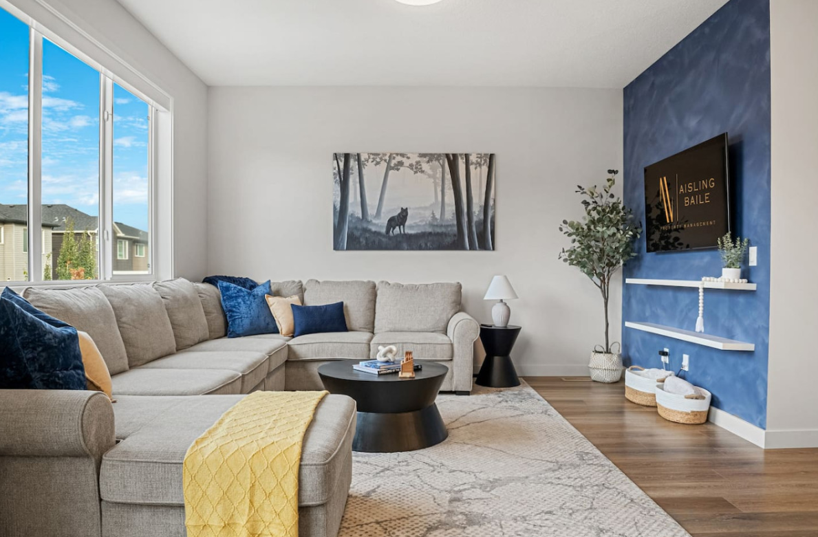 Modern living room with gray sectional, blue accent wall, fireplace TV, and large windows