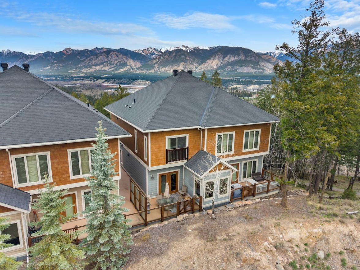 Two-story house with gray roof and mountain view, surrounded by trees and dry yard