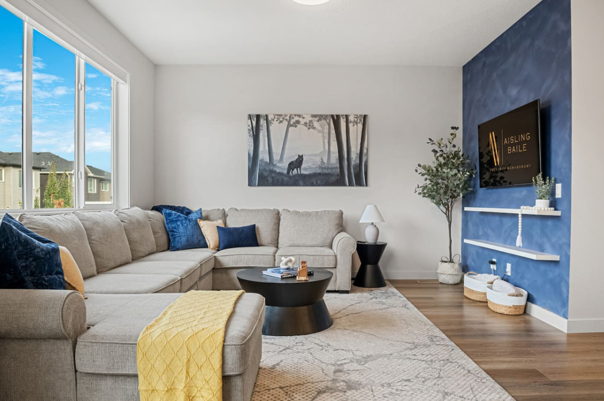 Modern living room with gray sectional, blue accent wall, TV, and large window with city view