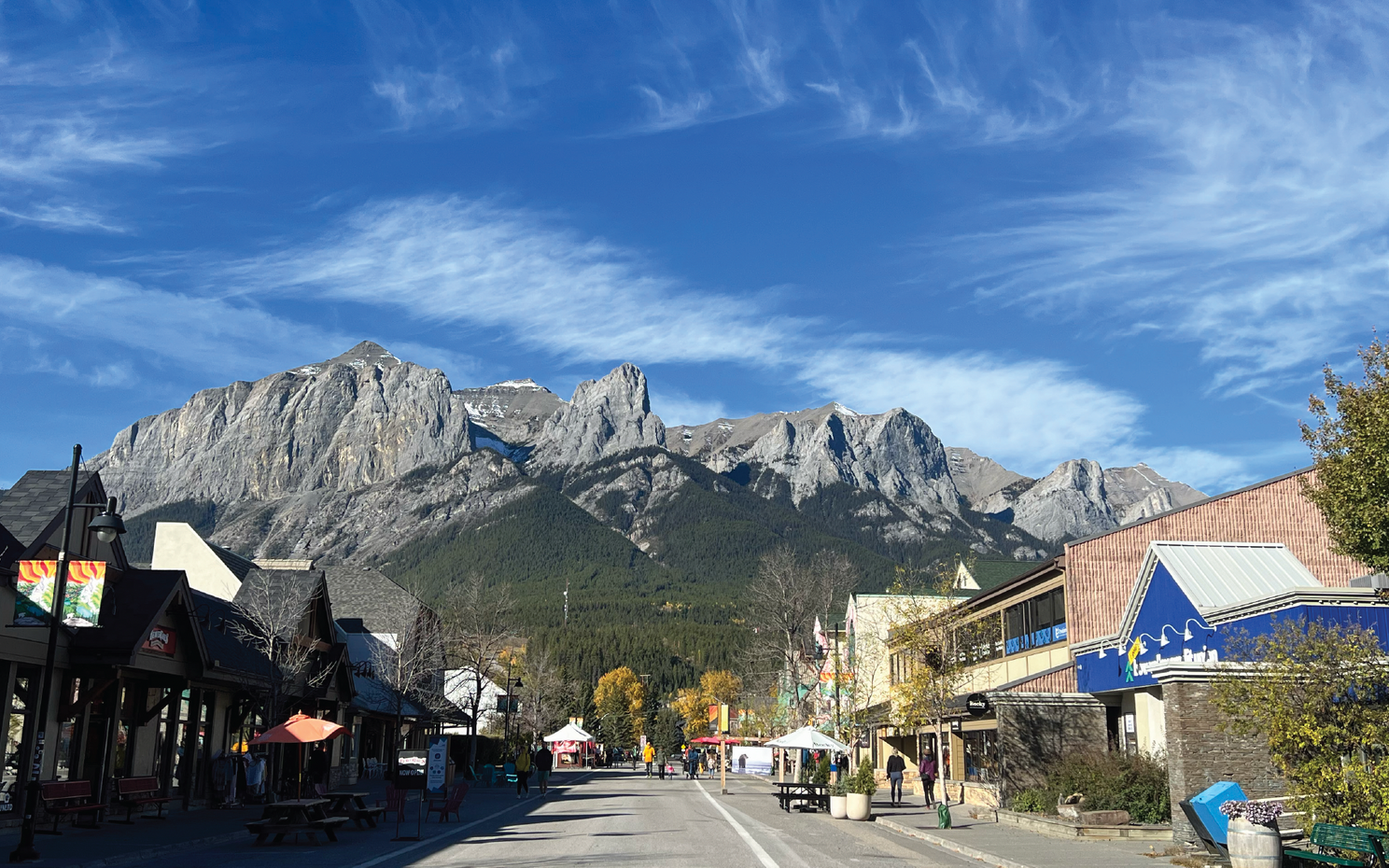 Street view with shops and a mountain backdrop under a blue sky.