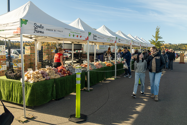 Outdoor market stalls with white tents and shoppers browsing produce on a sunny day