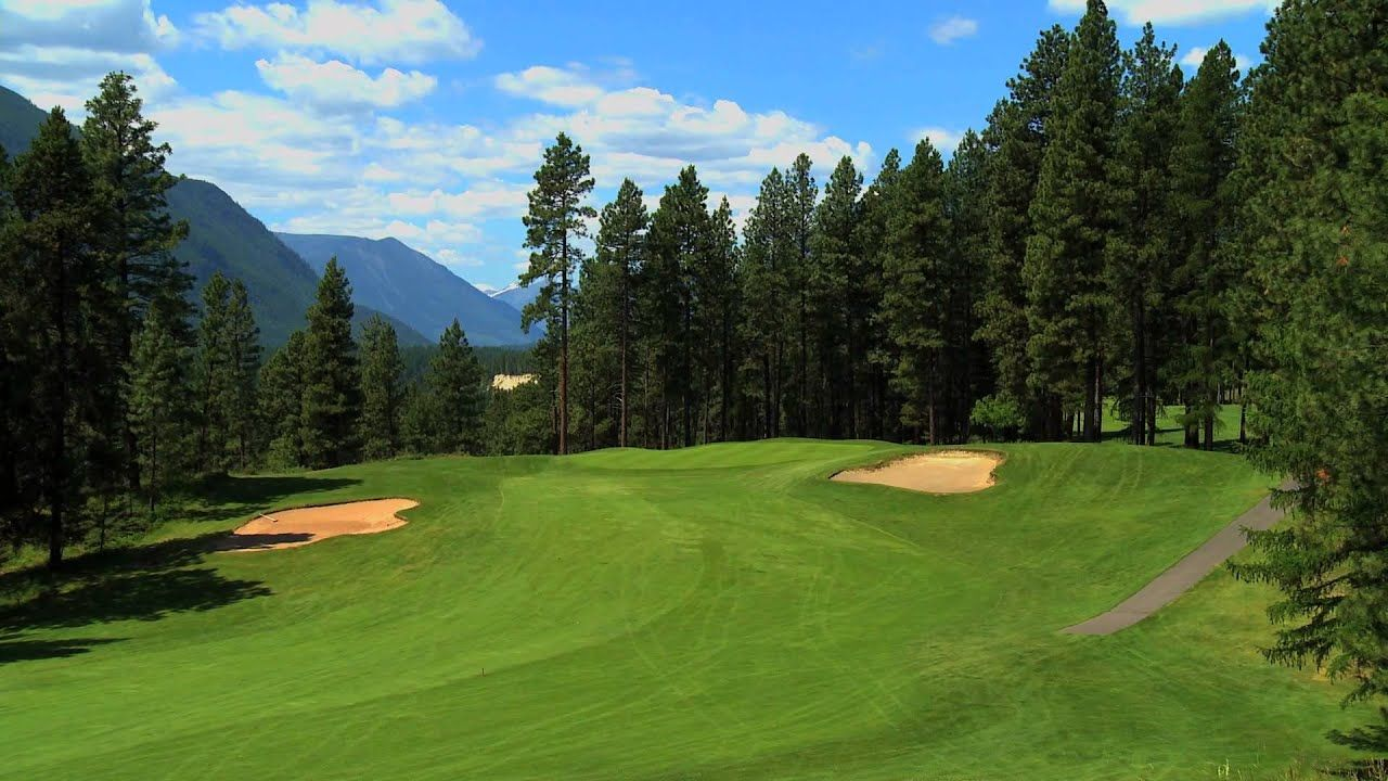 Golf course fairway surrounded by pine trees and mountains under a clear blue sky