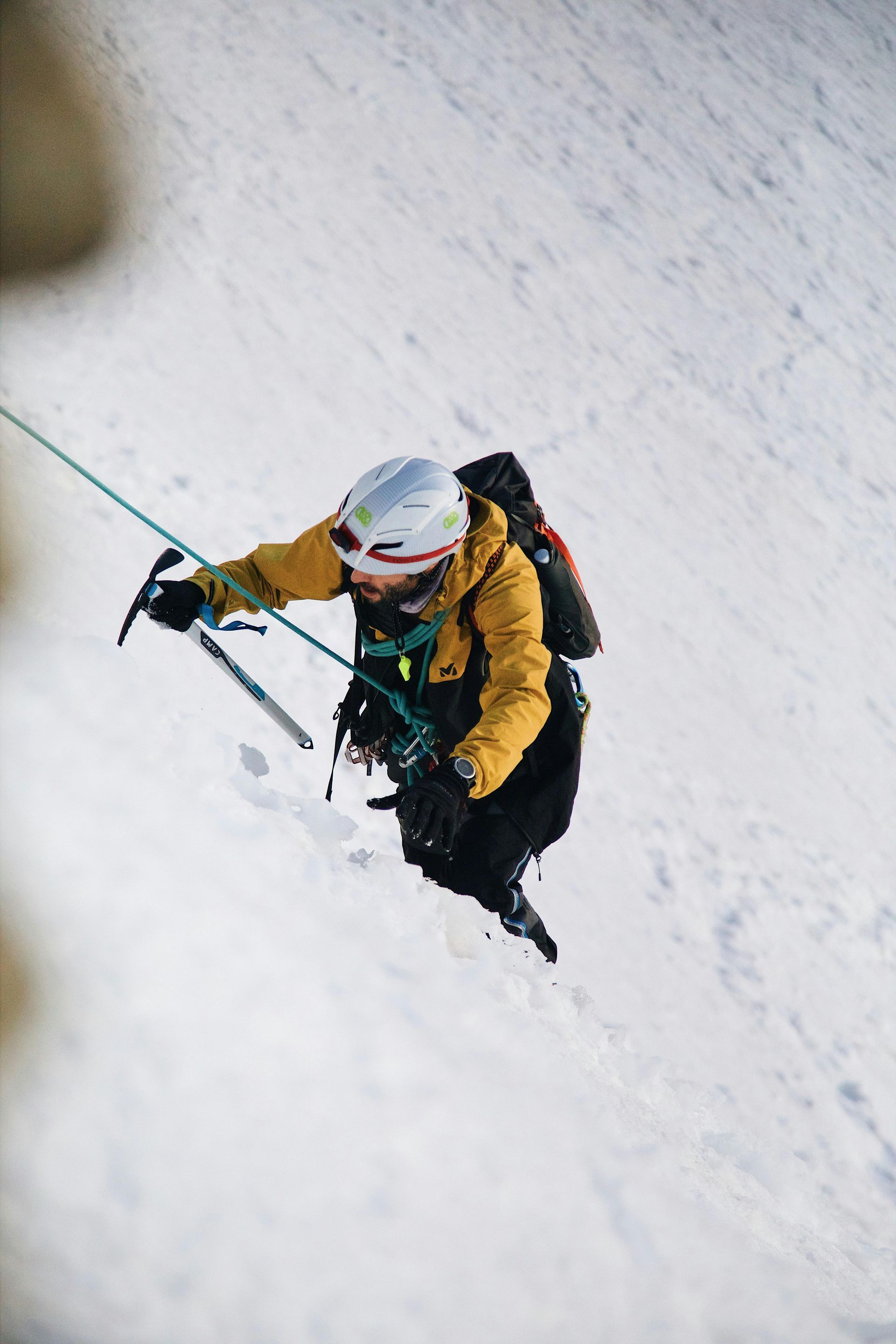 Person in yellow jacket ice climbing a snowy mountain face, secured by a rope.