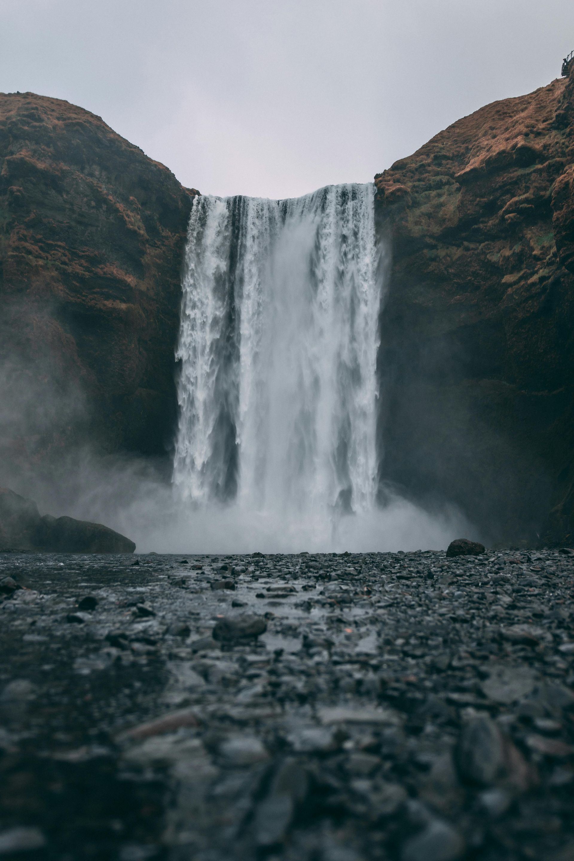 Waterfall cascading down rocky cliffs, misty spray. Gray sky, overcast.