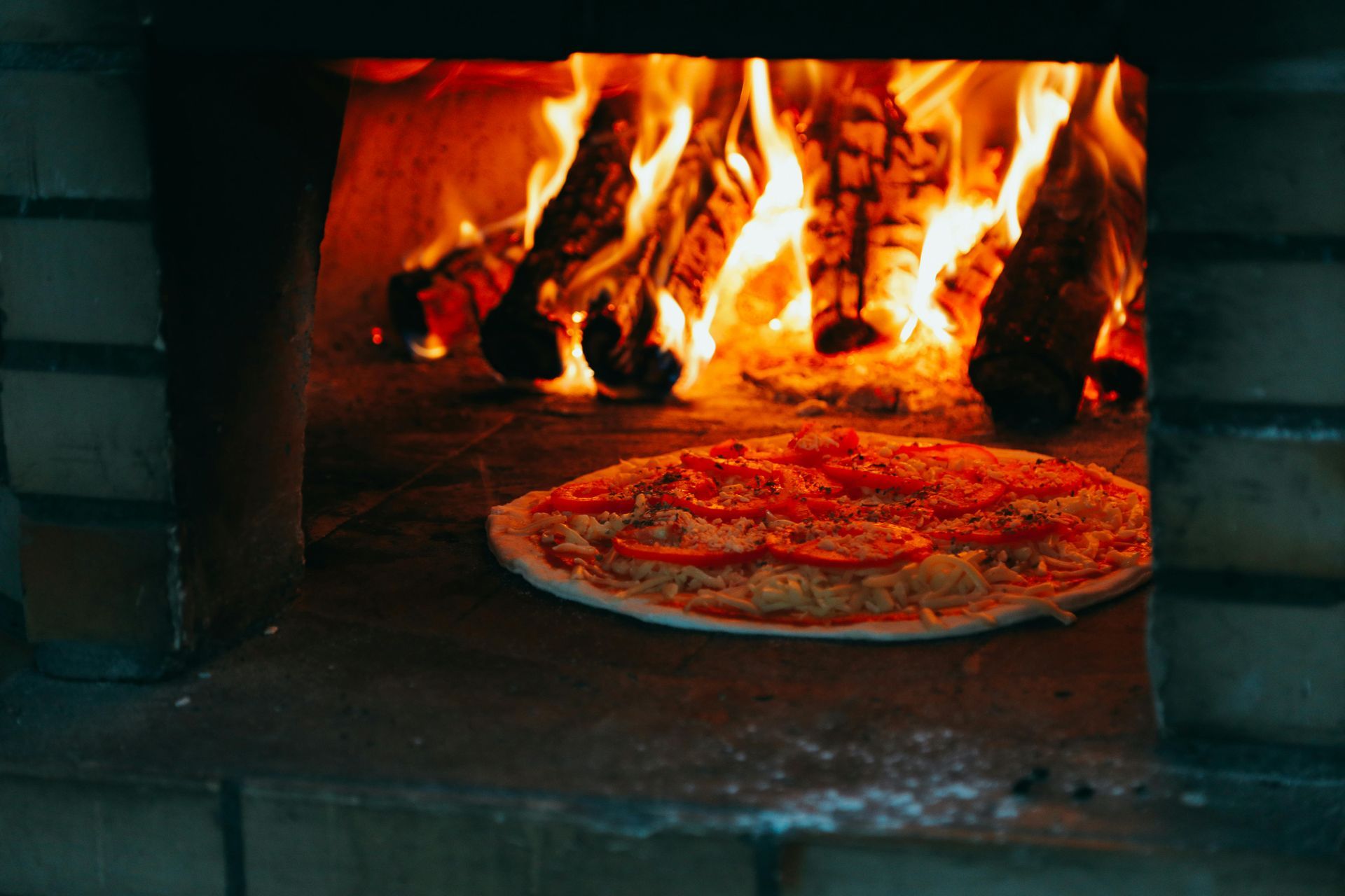 Pizza baking in a brick oven with a roaring fire.