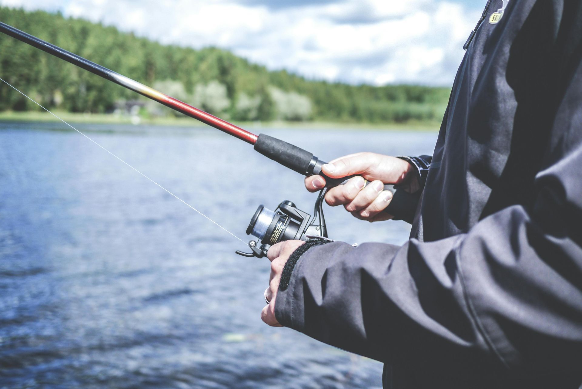 Person holding a fishing rod, preparing to cast into a lake with trees in the background.