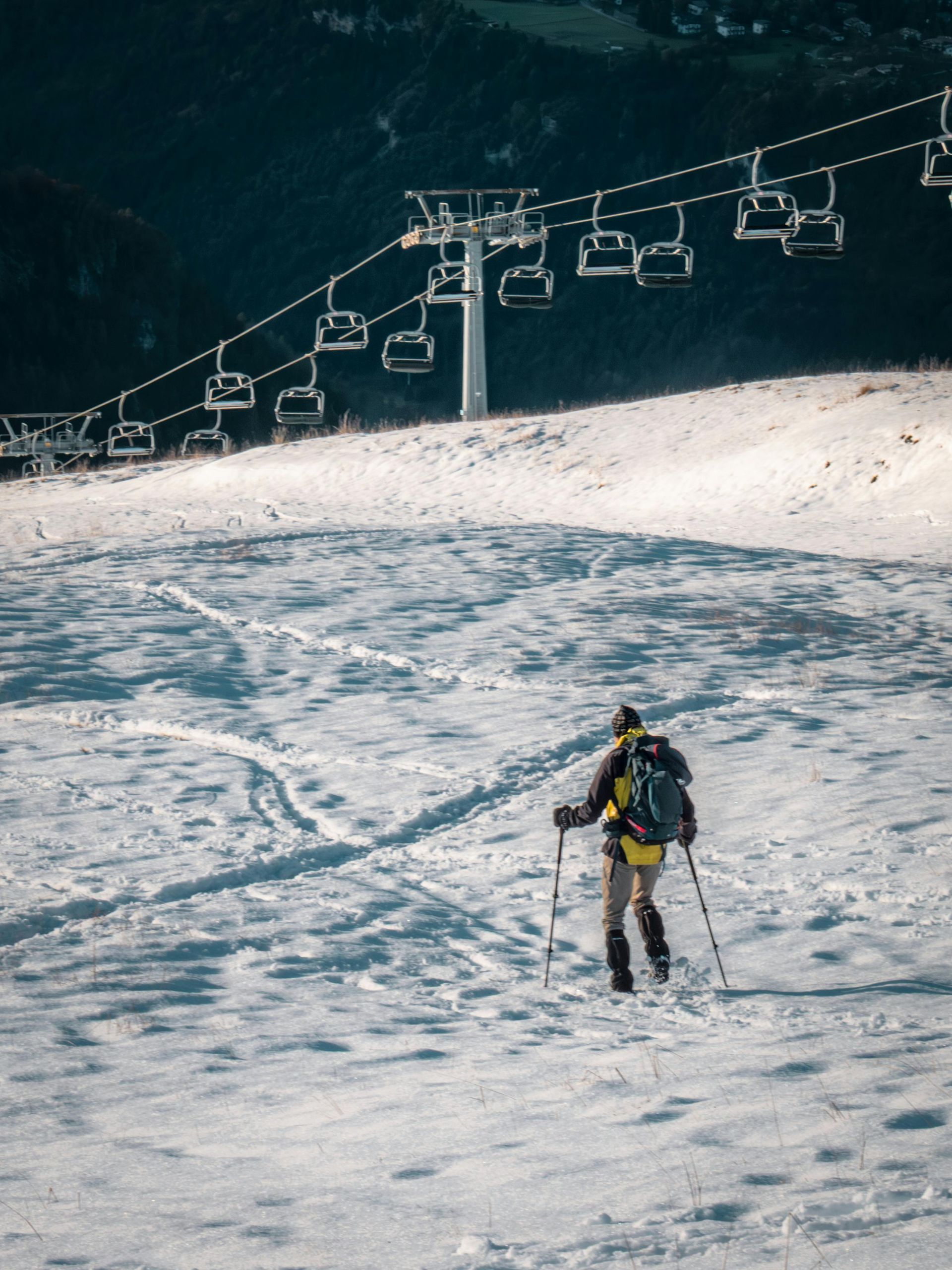 Person hiking up a snowy mountain slope with ski lift in the background.