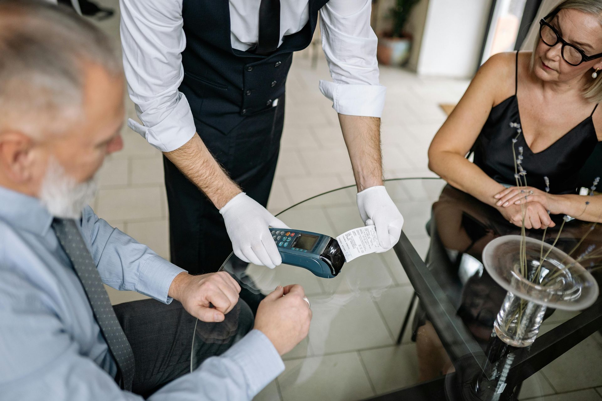 Waiter showing a payment terminal to a person at a table, another person beside.