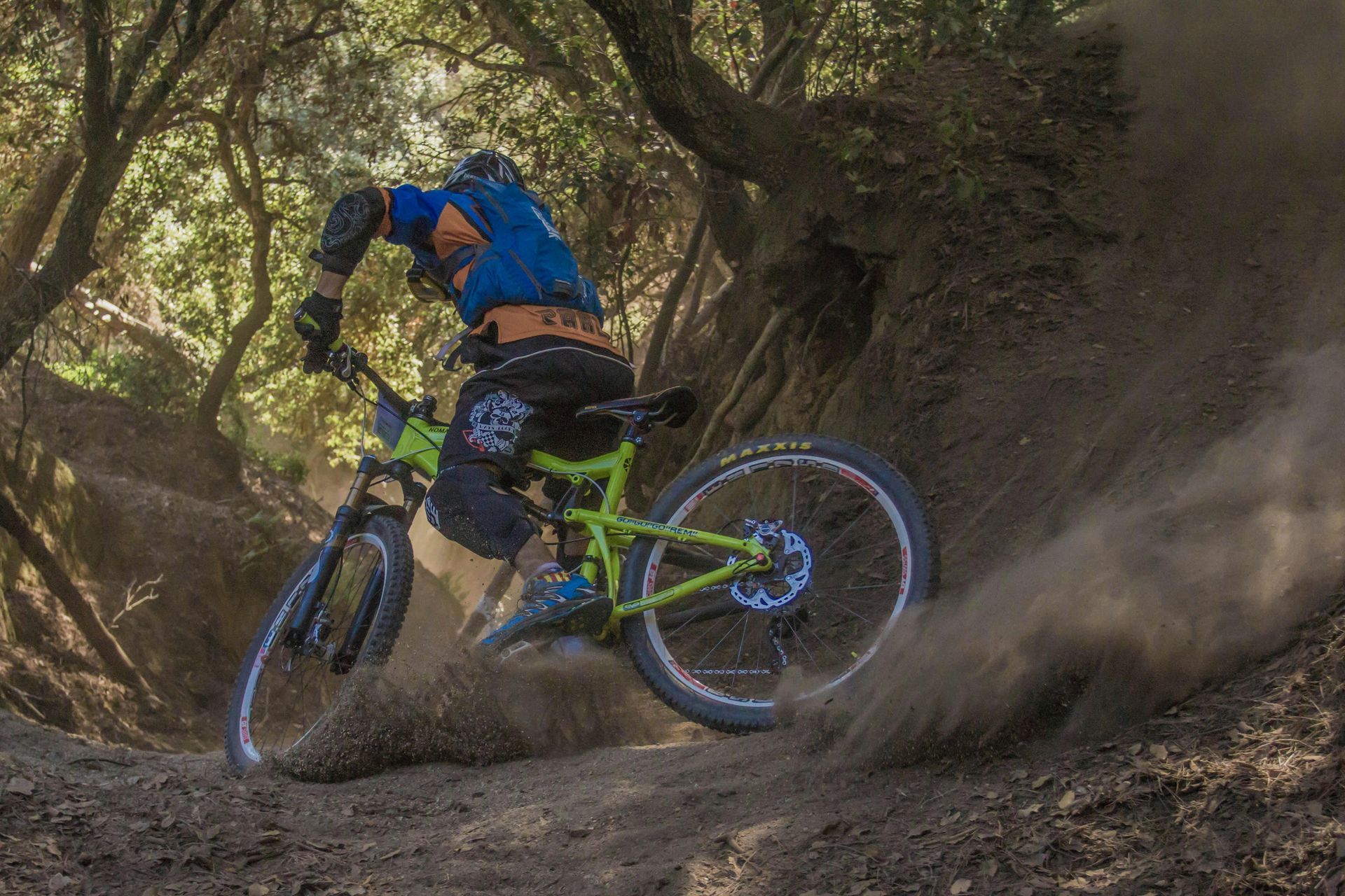 Mountain biker riding downhill on a dirt trail, kicking up dust.