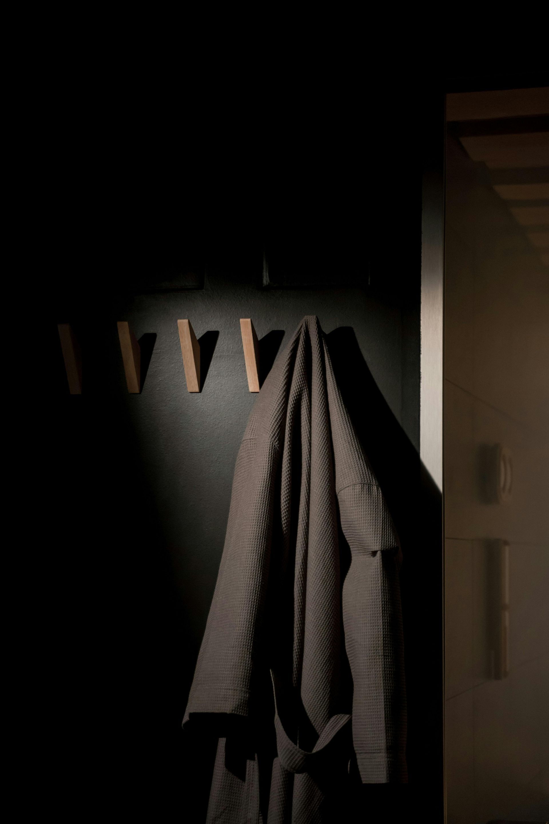 A dark room with a grey robe hanging on wooden pegs; adjacent to a light-colored door.