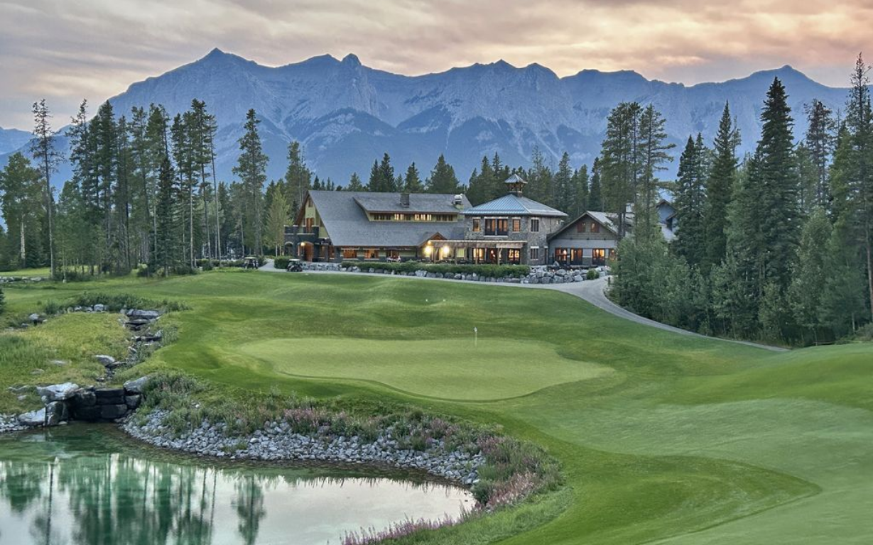 Golf course with a large lodge building and mountain backdrop at dusk.