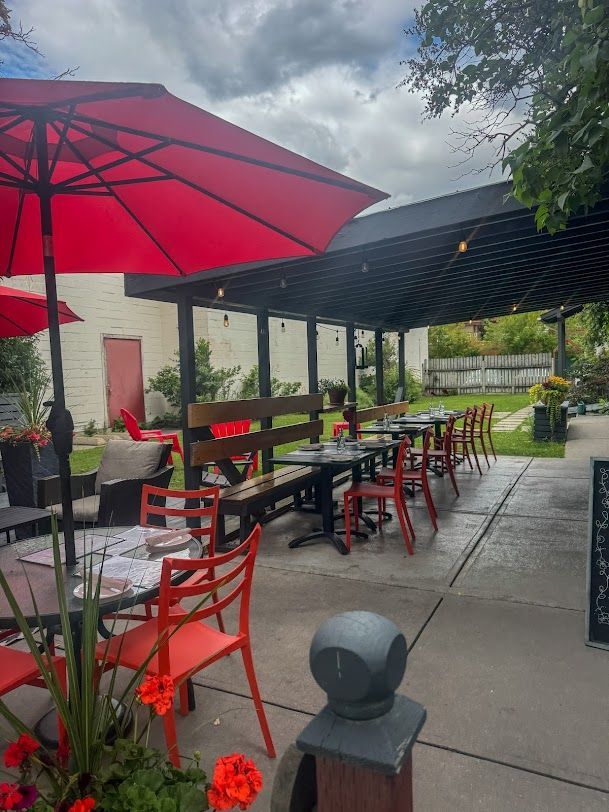 Outdoor restaurant patio with red umbrellas, tables, and chairs. Overcast sky.