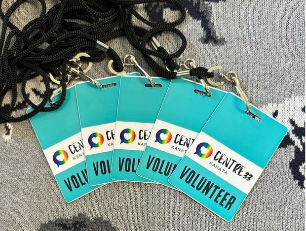 Four teal volunteer name badges with lanyards spread on a gray fabric surface