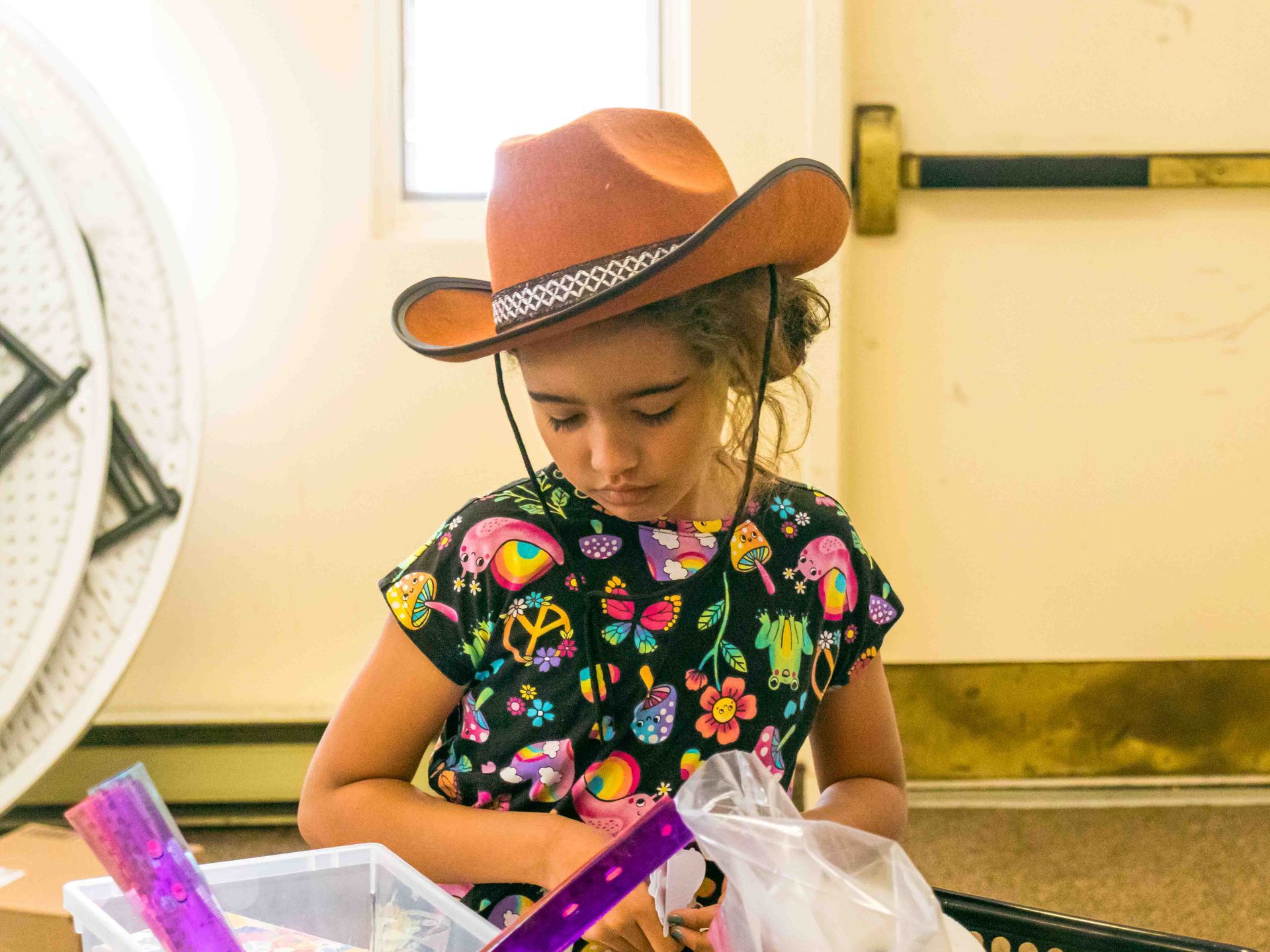Child in a cowboy hat opening a gift box at a table indoors