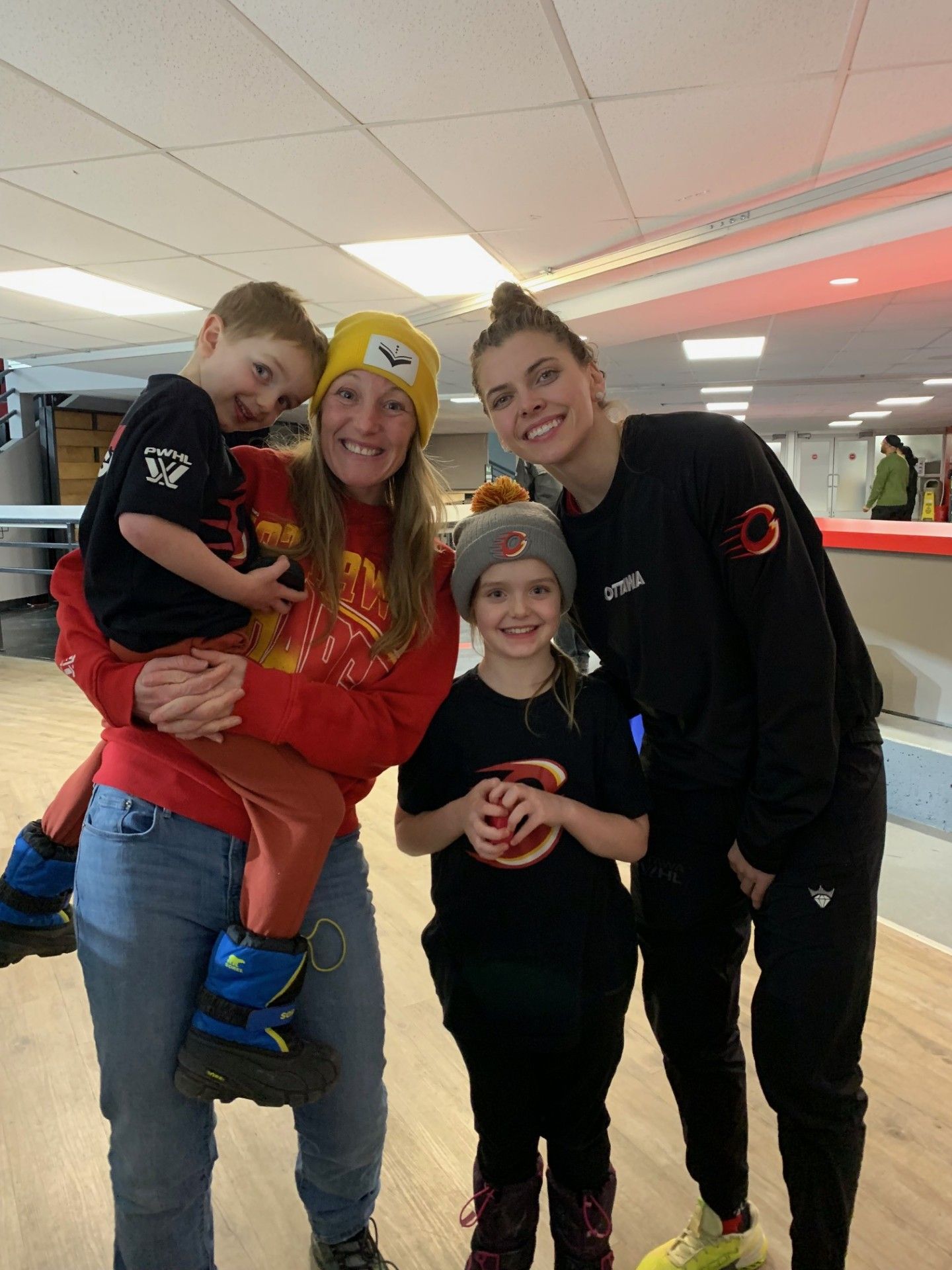 Four people smiling indoors at a bowling alley, posing together with bowling balls.