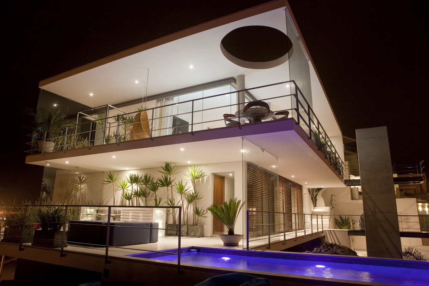 Una casa grande con piscina frente a ella por la noche.