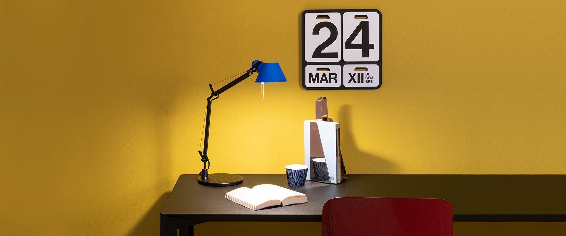 Un escritorio con una lámpara y un calendario en la pared