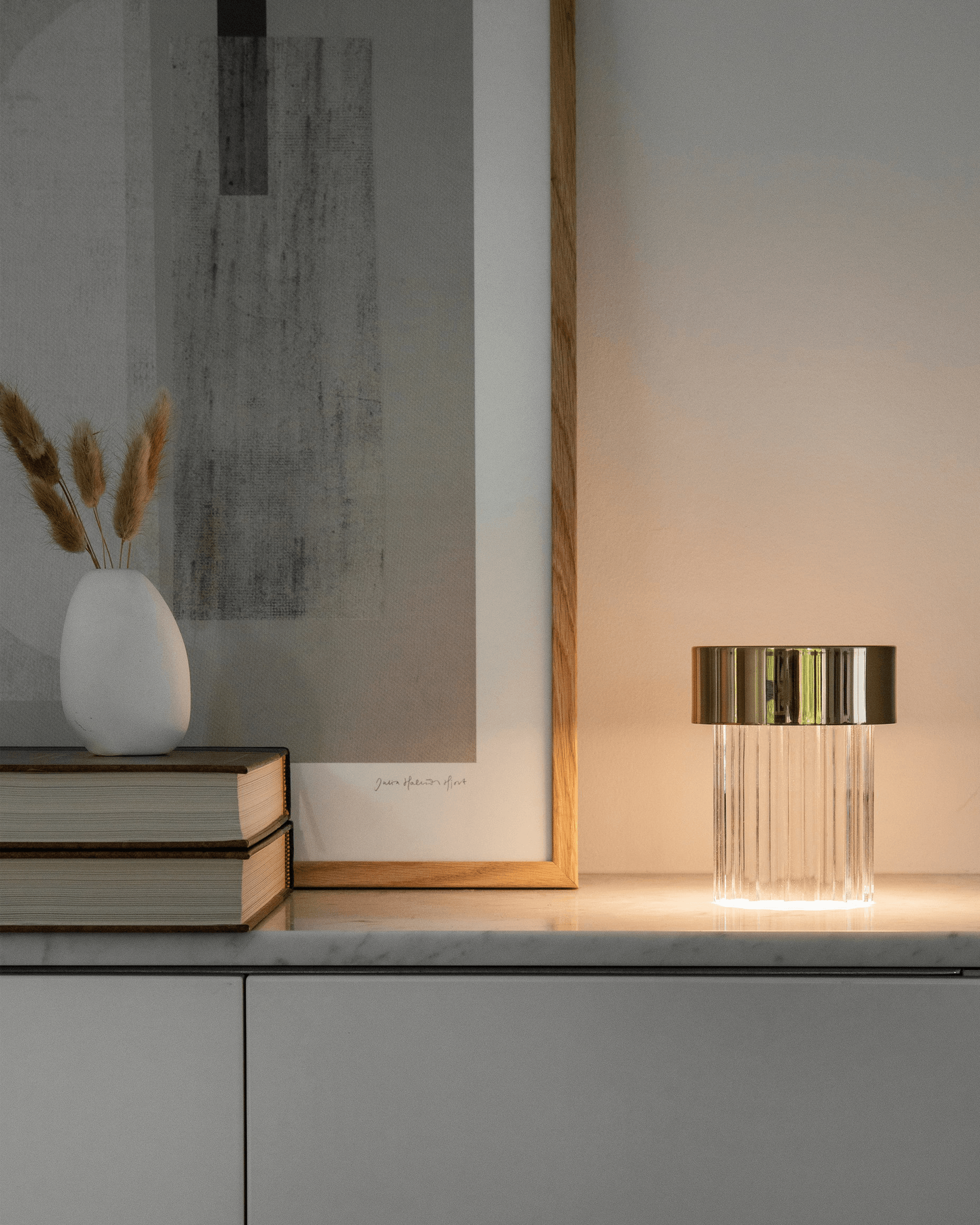 Hay una lámpara sobre una mesa junto a un cuadro y libros.