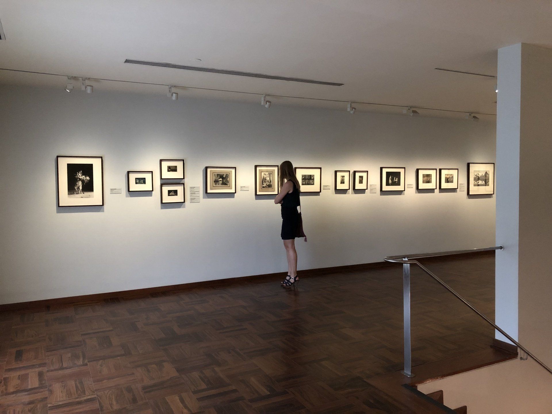 Una mujer con un vestido negro mira cuadros en una pared de un museo.