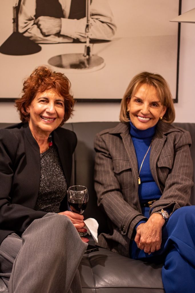 Dos mujeres están sentadas en un sofá sosteniendo copas de vino.