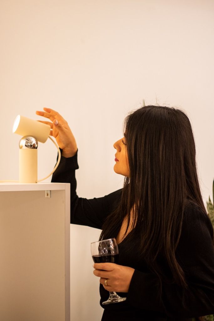 Una mujer sostiene una copa de vino y mira una lámpara.