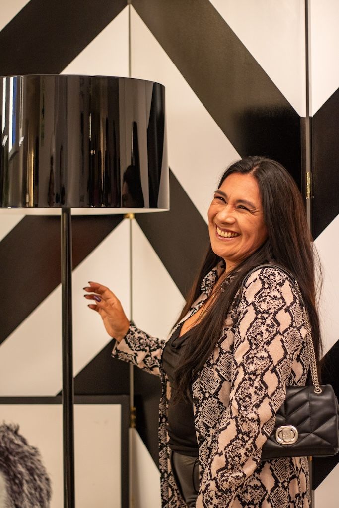 Una mujer está parada frente a una pared de rayas blancas y negras junto a una lámpara.