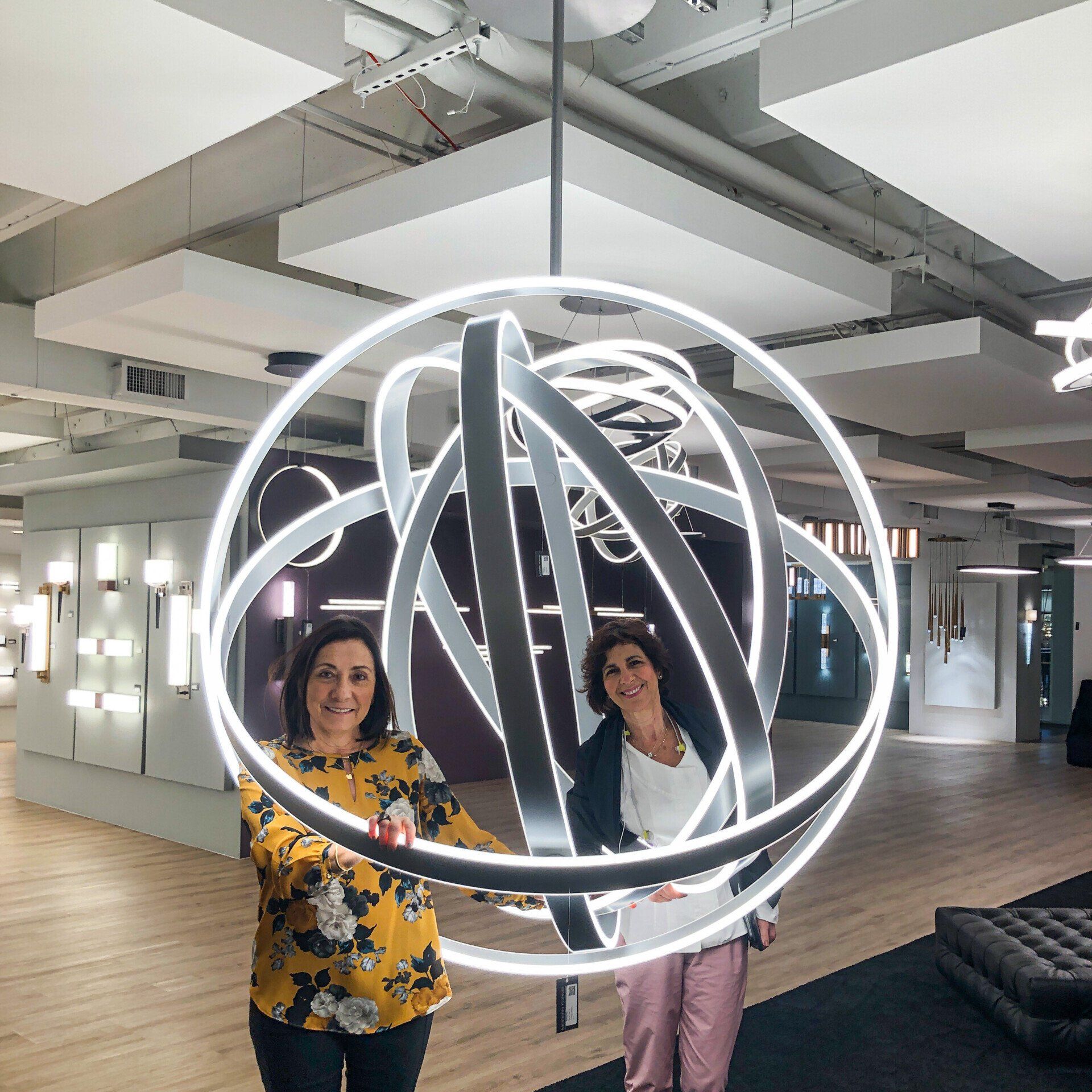 Dos mujeres están paradas una al lado de la otra sosteniendo una gran luz que cuelga del techo.