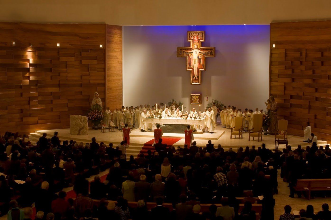 Un gran grupo de personas está sentada en una iglesia con una cruz en la pared.