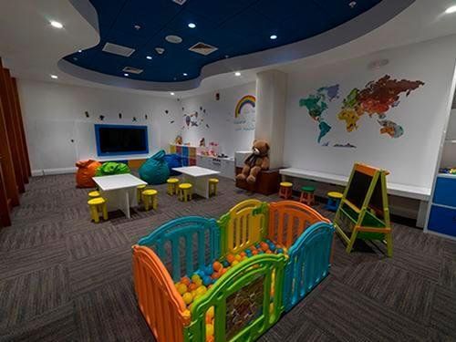 Una sala para niños con mesas, sillas, piscina de pelotas y televisión.