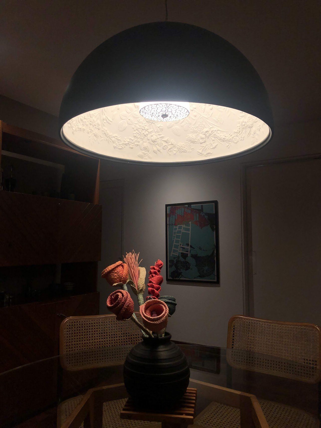 Una lámpara cuelga del techo sobre un jarrón de flores sobre una mesa.