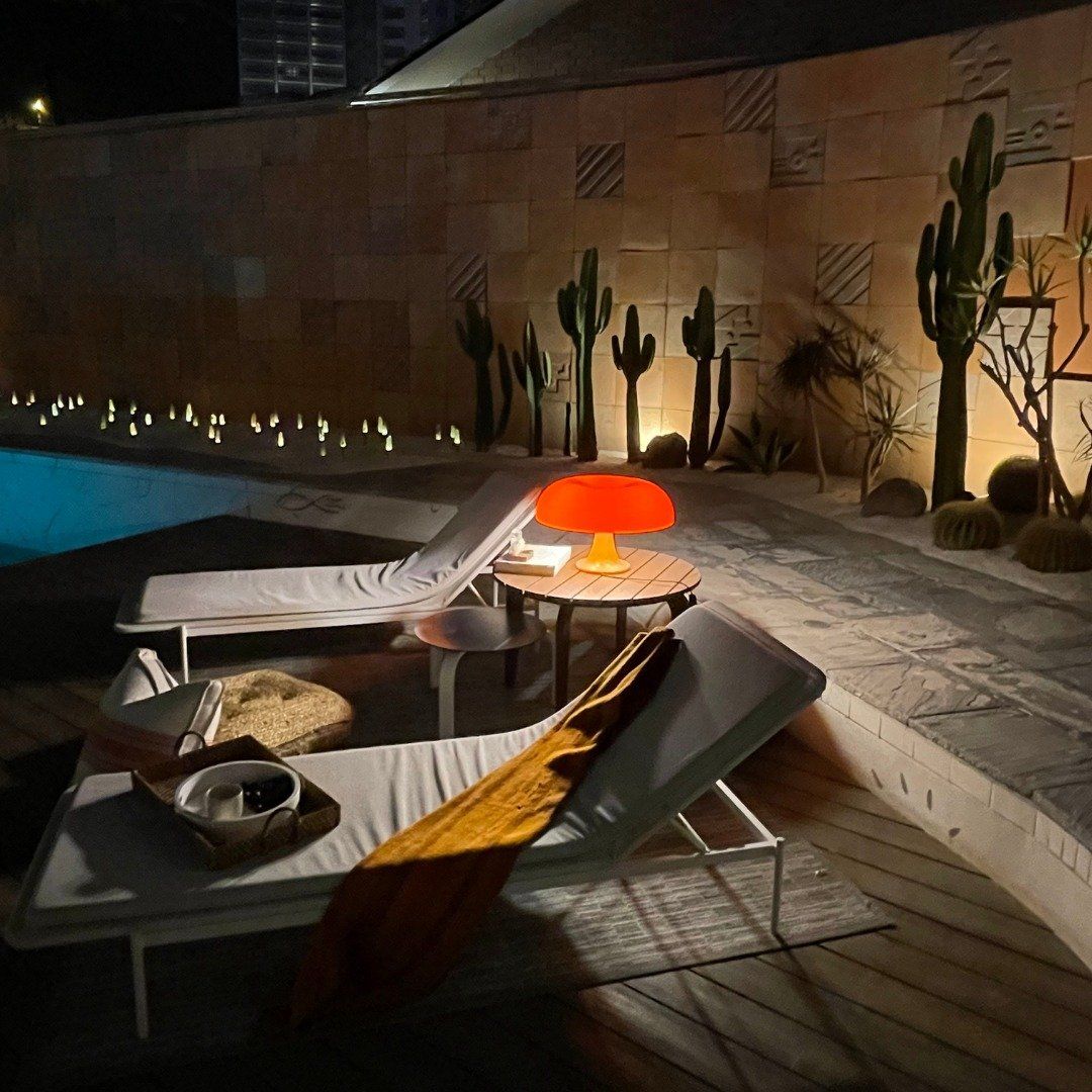 Una mesa con una lámpara encima frente a una piscina.