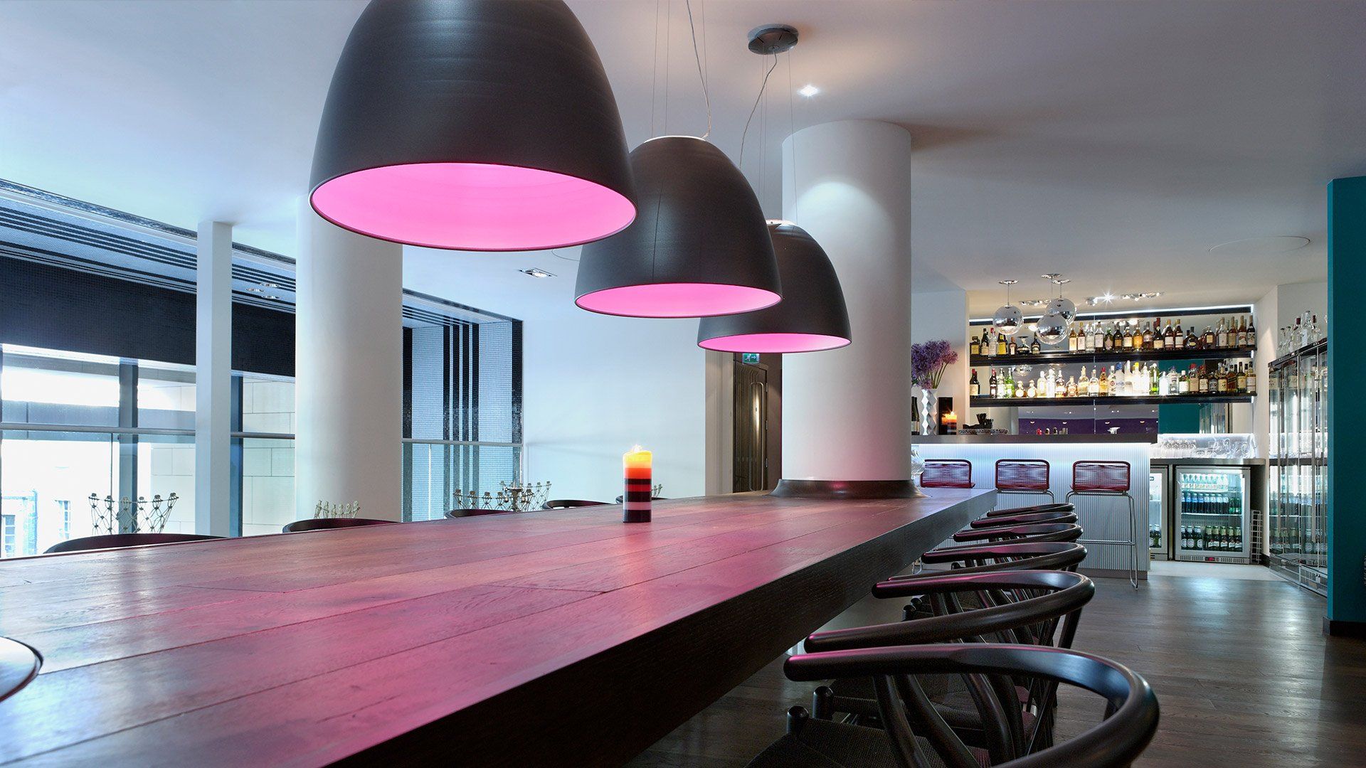 Una mesa larga de madera con luces rosas colgando del techo.