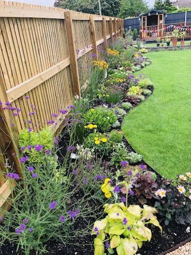 Colorful flower bed along a wooden fence beside a green lawn in a backyard