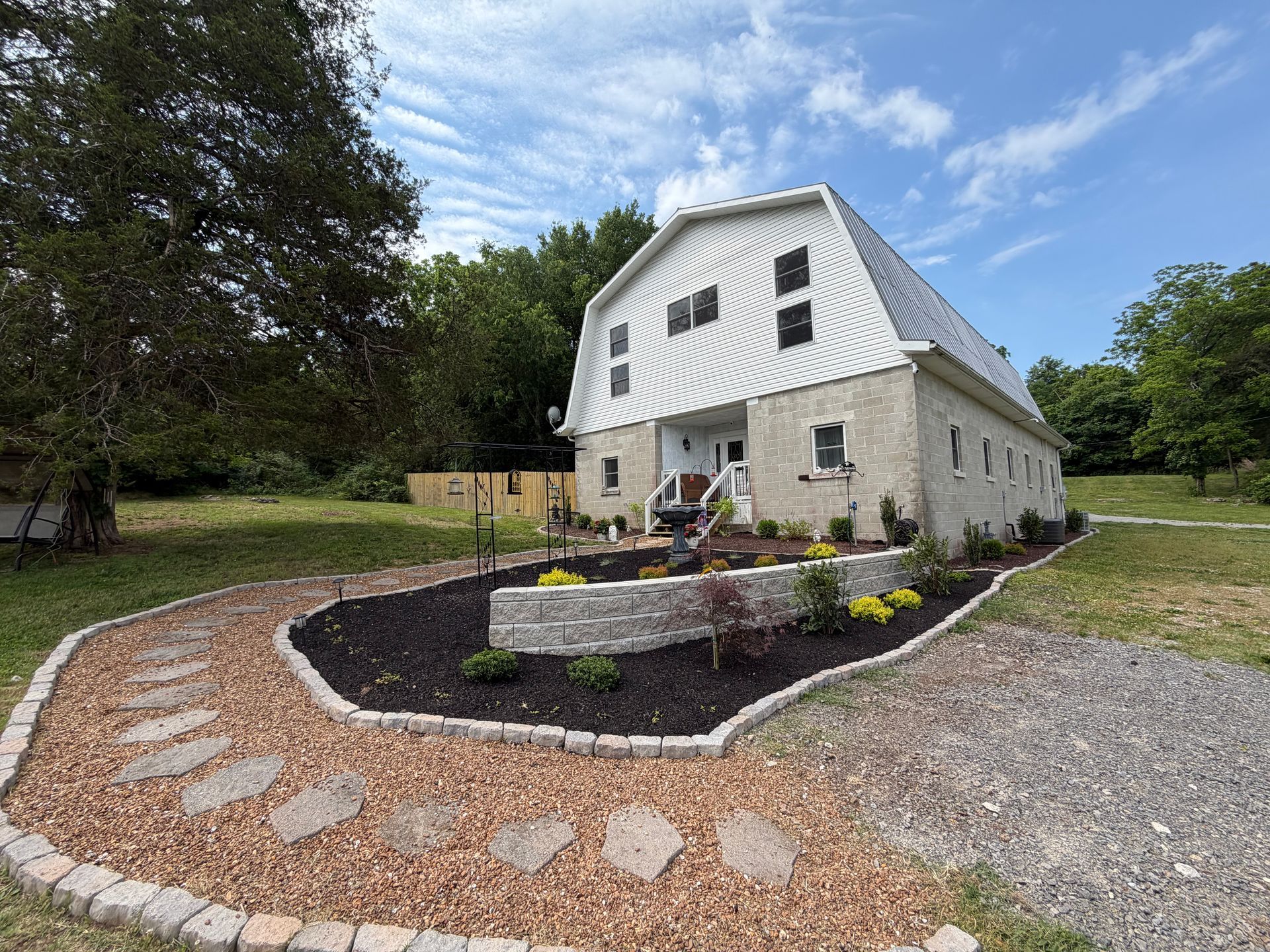 House with white upper story, stone lower level, and curved brick walkway in a landscaped yard