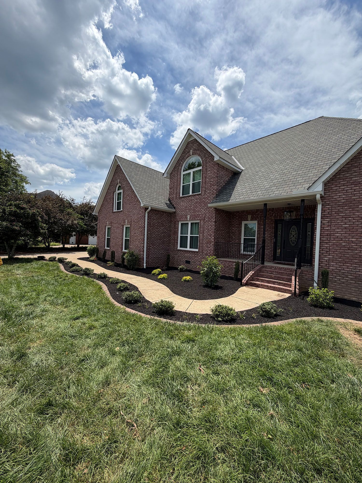 Brick suburban house with gray shingle roof, front lawn, and partly cloudy sky
