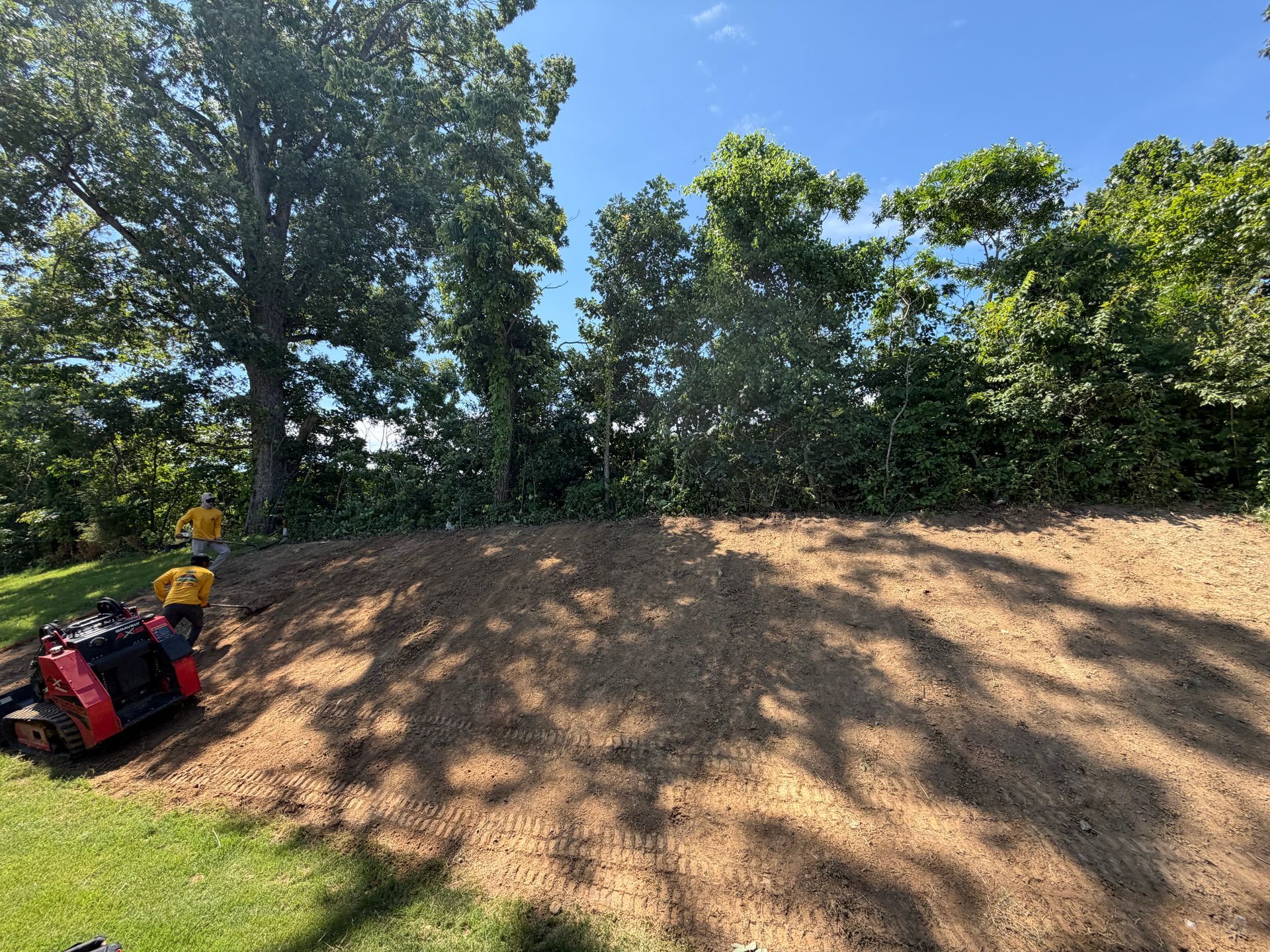 Backyard with fresh dirt trench beside a house and small deck, likely for construction or drainage work
