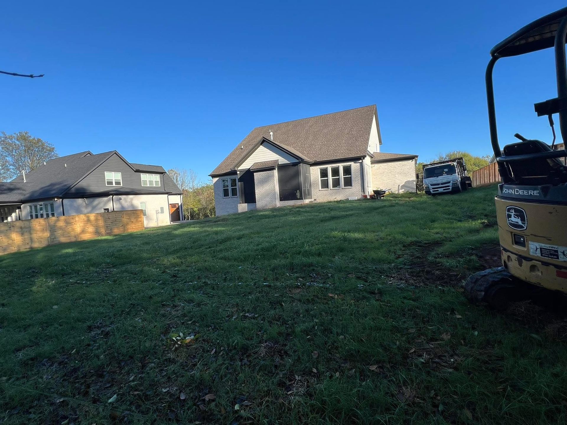 Patchy grass lawn beside a gray brick house with patio doors and a concrete patio.