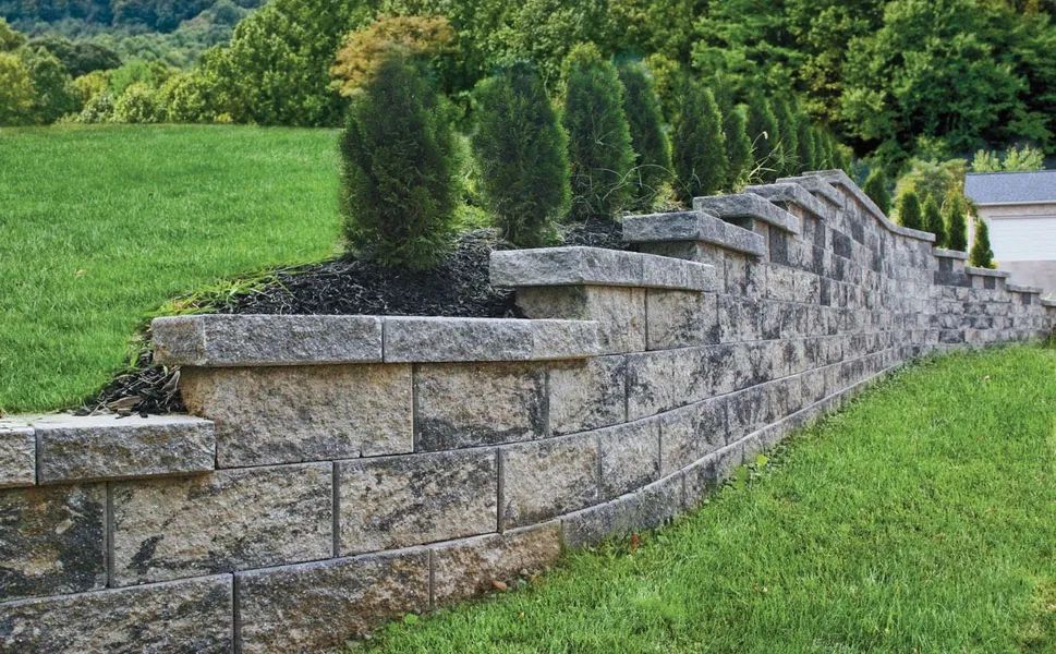 Curved stone retaining wall with small shrubs along a grassy landscape