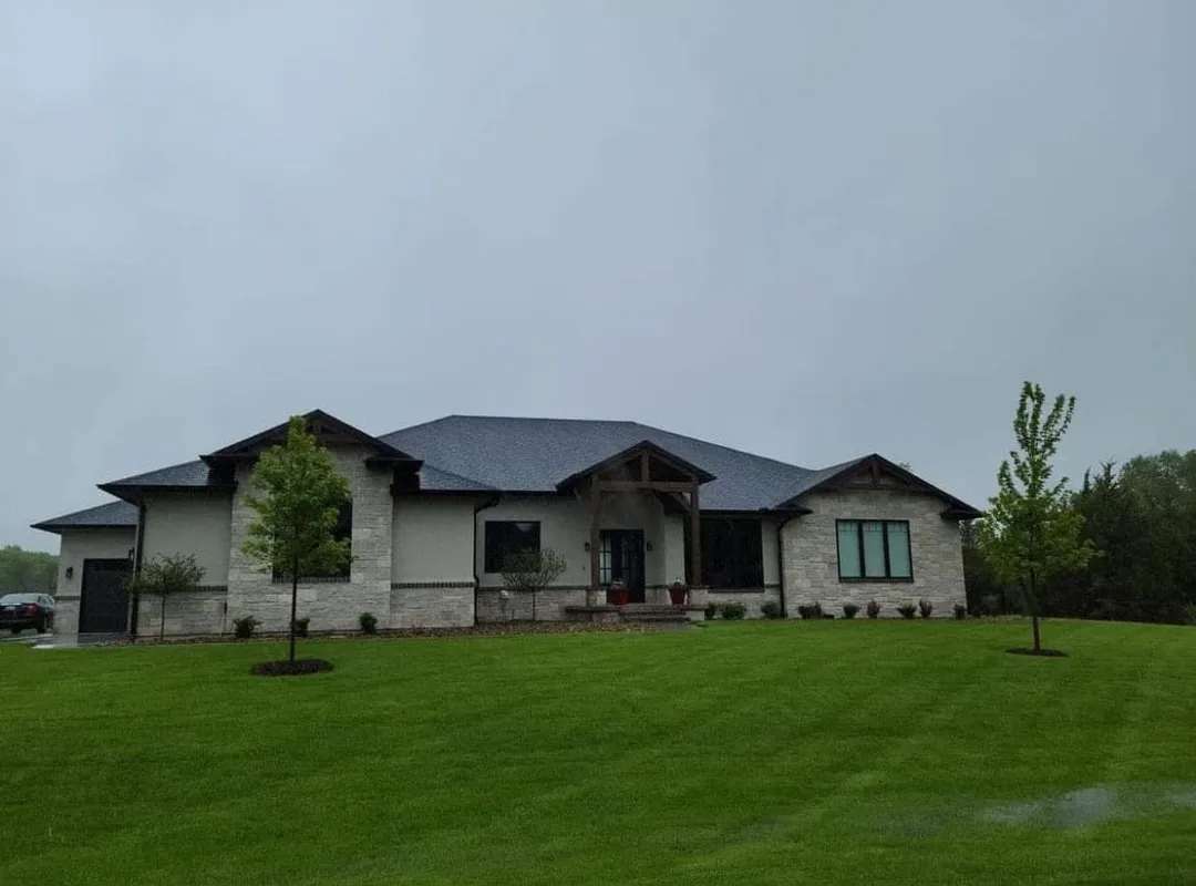 Single-story house with dark roof on a green lawn under an overcast sky