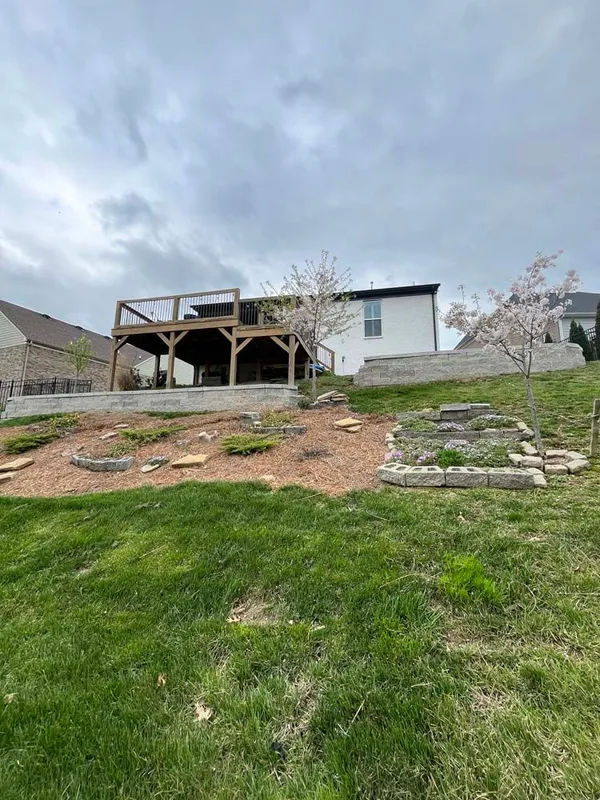 Suburban house with wooden deck, stone steps, and sloped green yard under cloudy sky