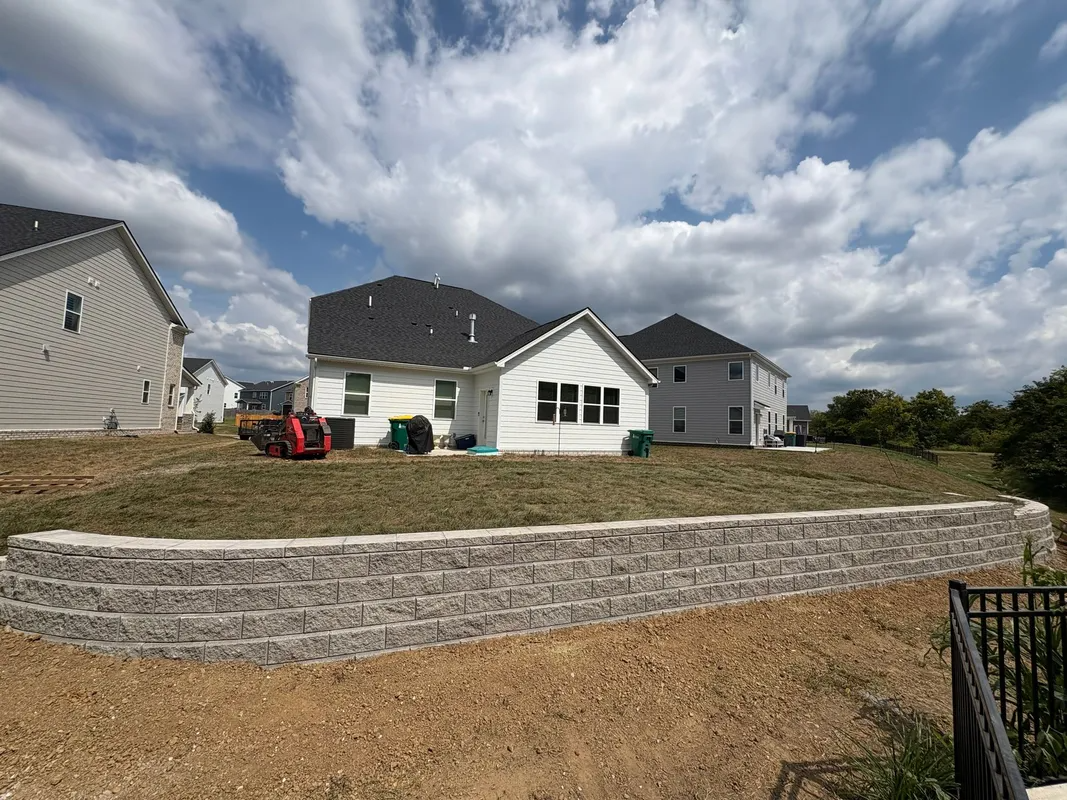 Suburban backyard with new houses, stone retaining wall, and cloudy sky