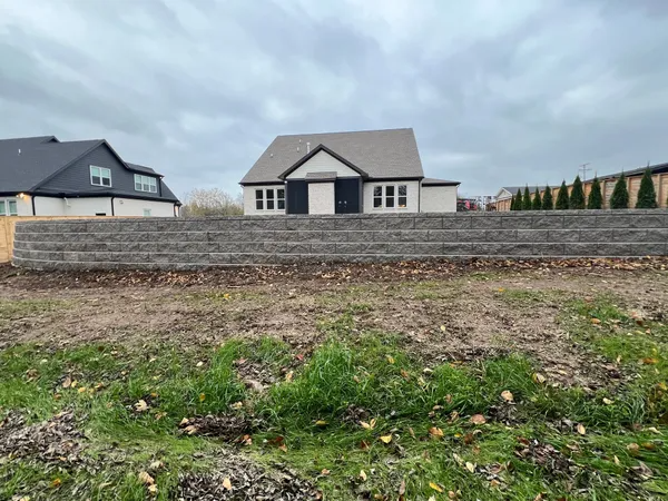 New suburban house behind a stone wall under cloudy sky