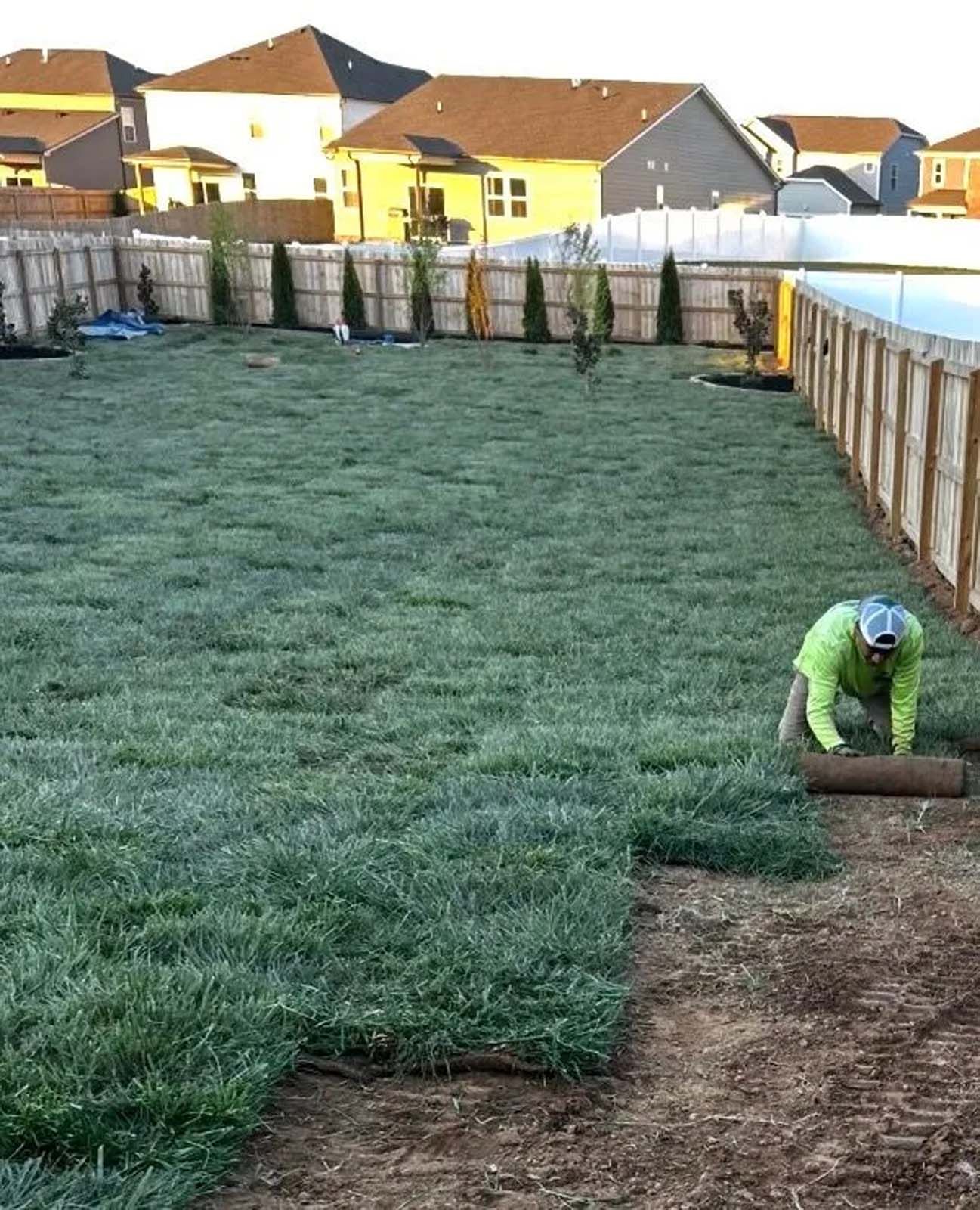 Worker rolling sod in a backyard lawn installation